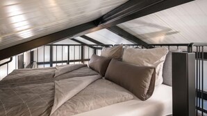 A bedroom with a sloped ceiling, a bed with a beige bedspread, and a window providing natural light.
