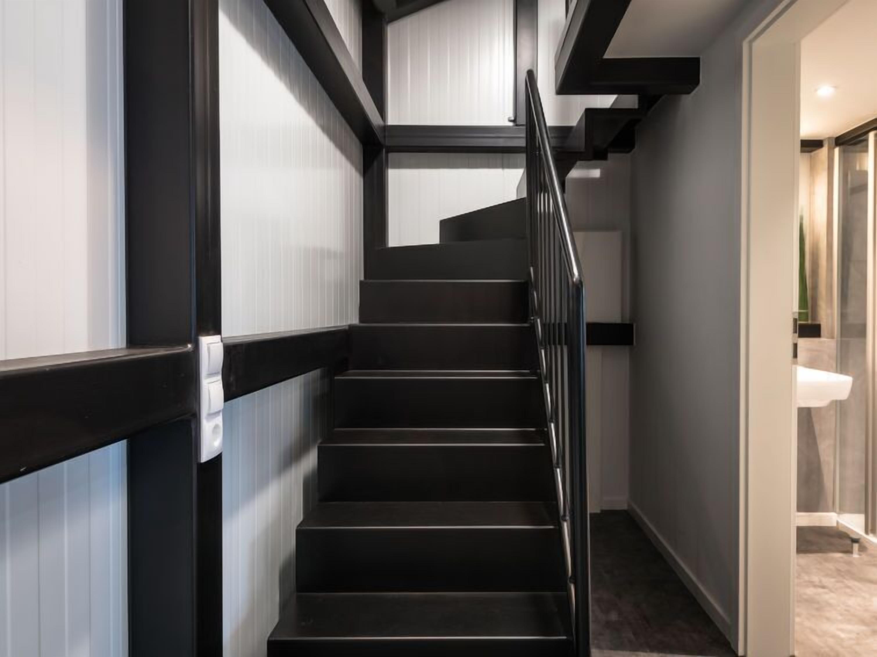 A modern staircase with black steps and metal railings, leading to a room with a white sink and a glass door.