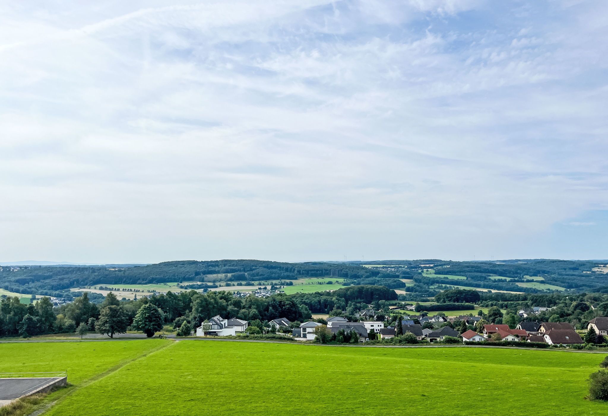 Ländliche Landschaft mit einer kleinen Häufung von Häusern, umgeben von grünen Feldern und Bäumen.