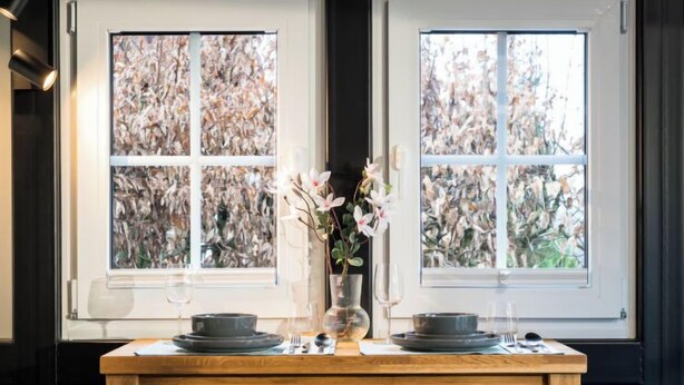 A wooden dining table with a vase of flowers, plates, and glasses set for two. - Tiny Haus Westerwald 16 Green by Interhome (Bad Marienberg)