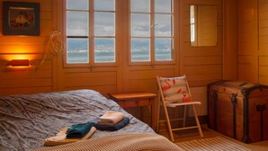 Una camera accogliente con un letto, una sedia, una valigia e un'ampia finestra vista mare.