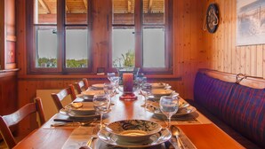 Una sala da pranzo in legno con tavolo apparecchiato per quattro persone, ampie finestre e una panca.