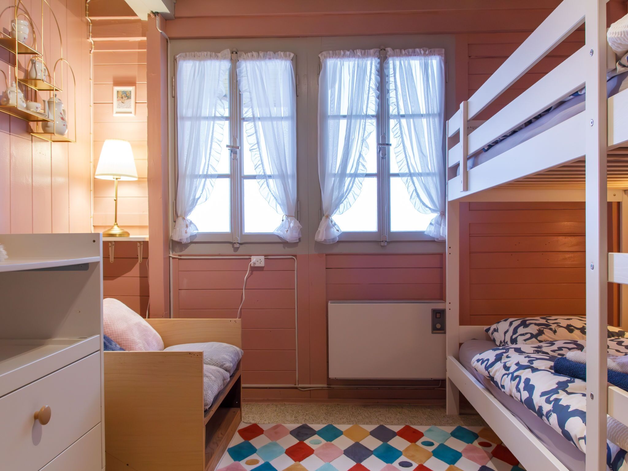 Een gezellige kamer met stapelbedden, een klein bureau en een raam met dunne gordijnen.