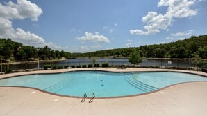 Uma piscina grande e vazia, com um céu azul límpido e uma colina arborizada ao fundo.