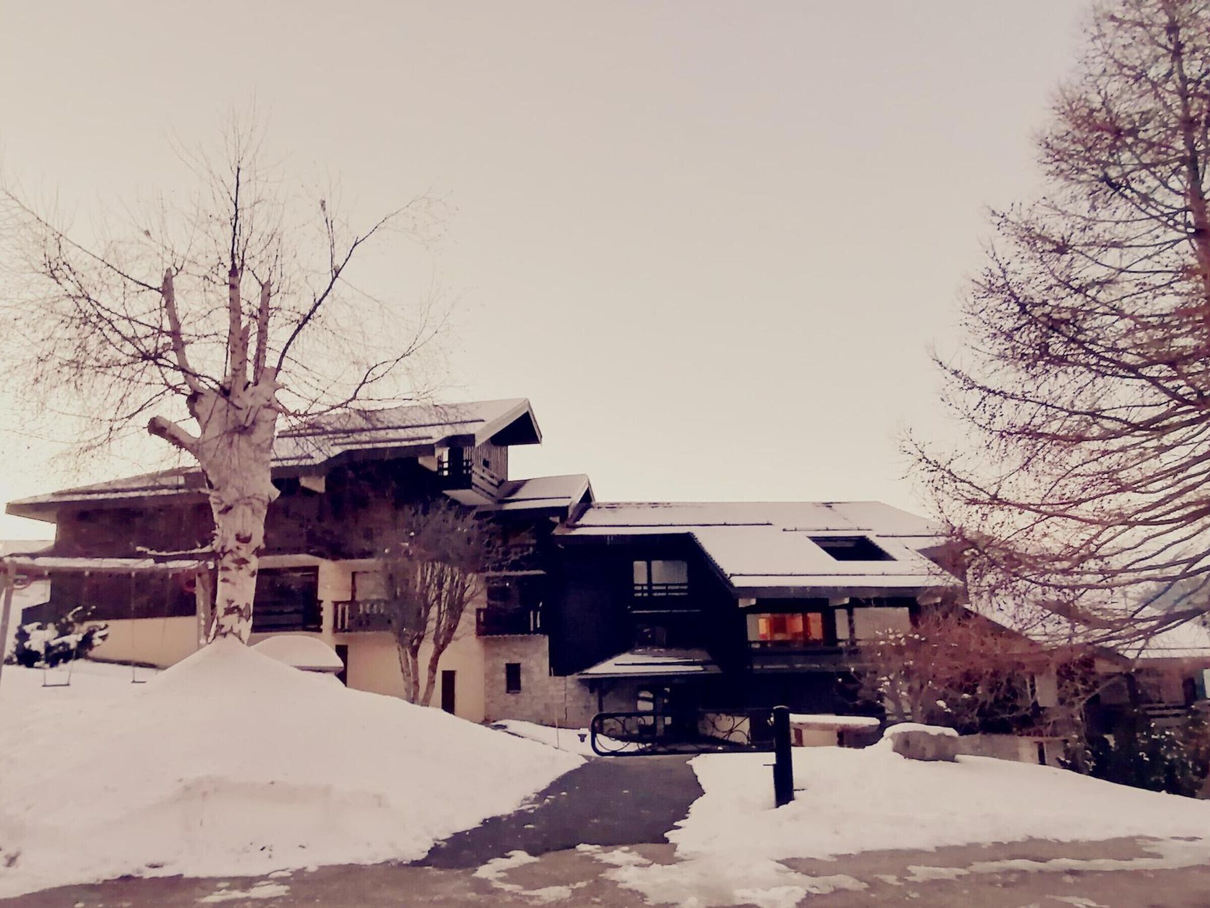 A modern building with multiple levels and a sloped roof, surrounded by snow-covered ground and leafless trees.