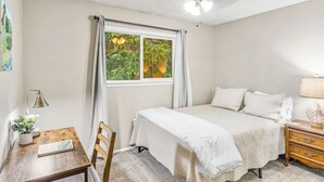 Un dormitorio con cama, escritorio, silla, lámpara y ventana con cortinas.