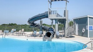 Una piscina con tobogán de agua, sillas de descanso y una torre de salvavidas.