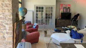 A living room with a stone wall, a globe, a painting, a red sofa, a white sofa, a television, and a person vacuuming. - Maison Méridional au Coeur D'uzès (Uzès)