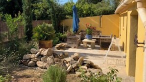 A garden with a yellow building, potted plants, and a stone wall. - Maison Méridional au Coeur D'uzès (Uzès)