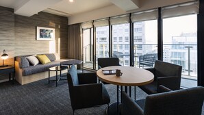Et moderne hotelværelse med sofa, stole, et bord og store vinduer med udsigt over byen.