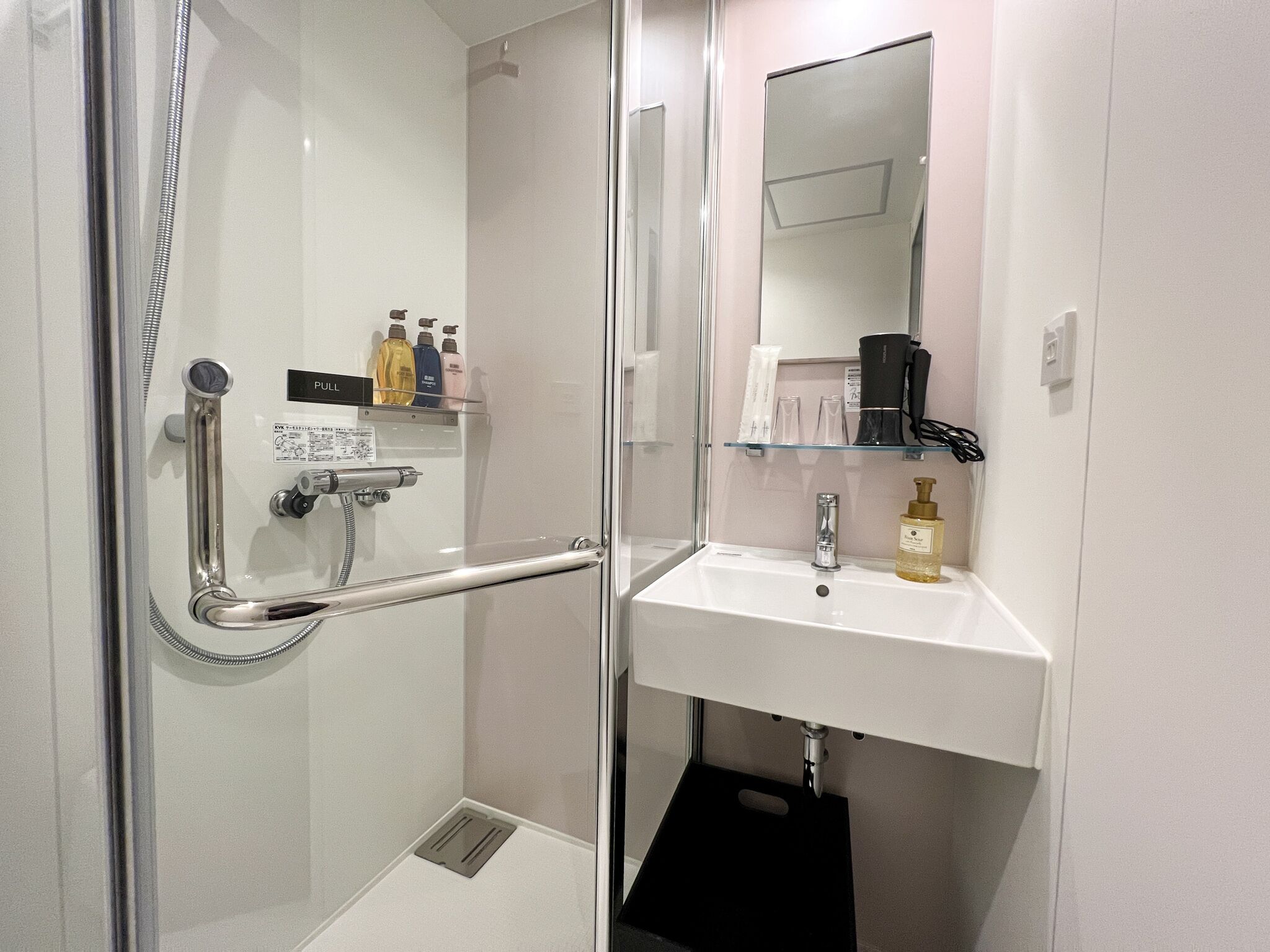 A modern bathroom with a glass shower enclosure, a white sink, and a mirror above it.