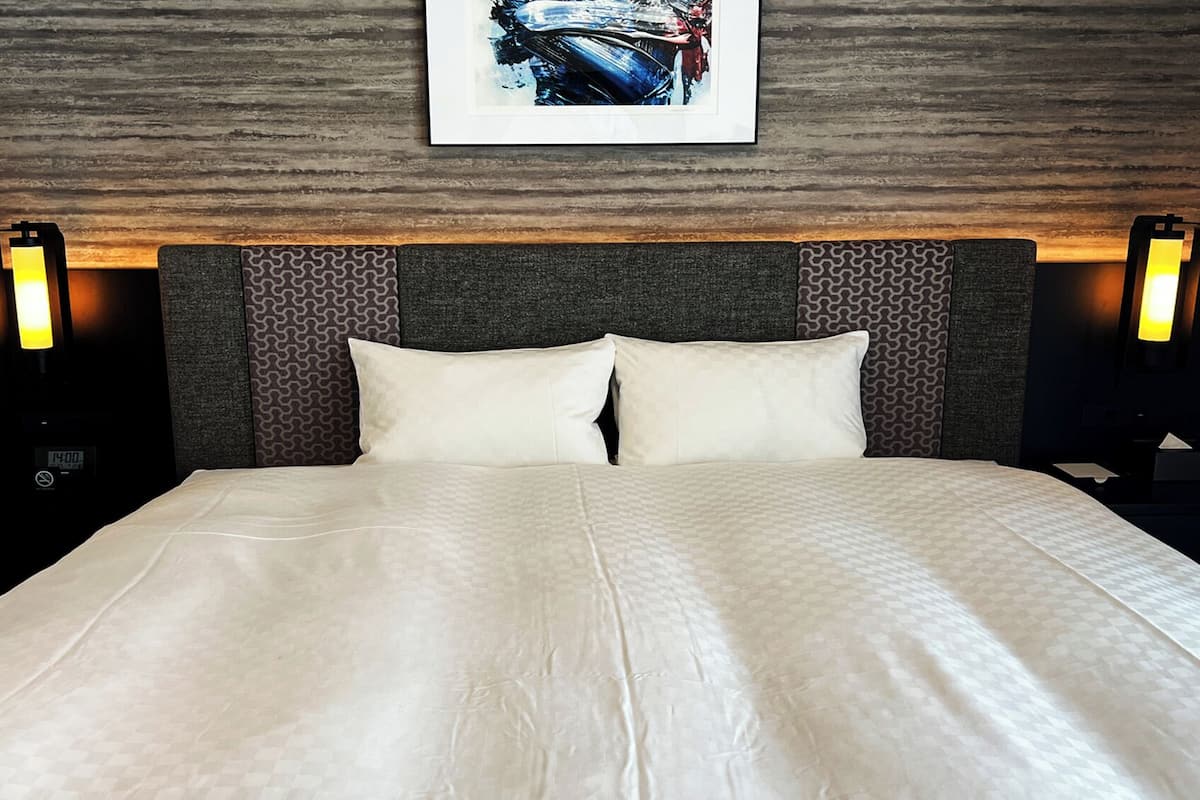 A neatly made bed with a patterned bedspread, a headboard with a geometric design, and two bedside lamps.