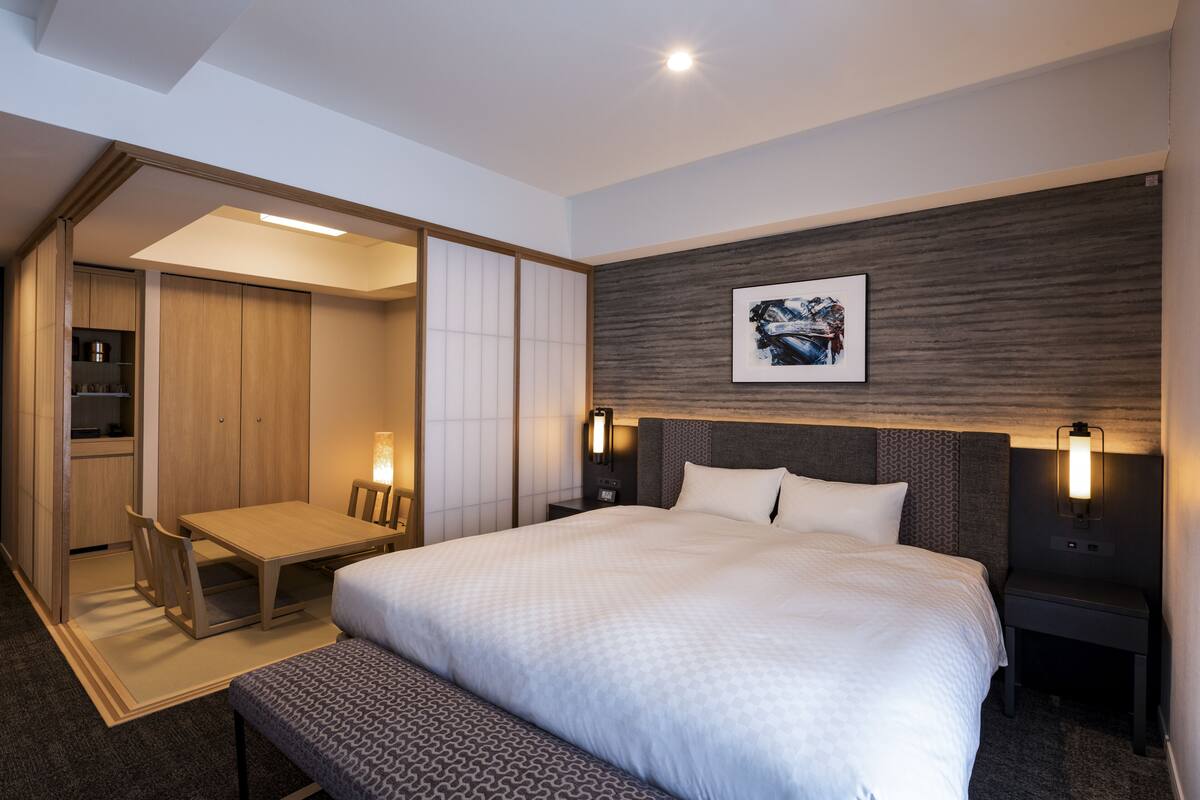 A modern hotel room with a large bed, bedside tables, a desk, and a bench.