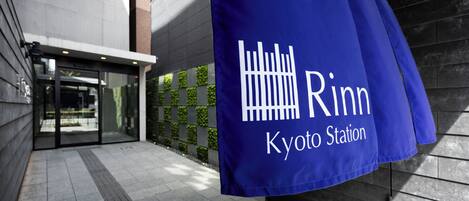 A blue banner with 'Rinn Kyoto Station' text, a modern building entrance, and a tiled walkway.