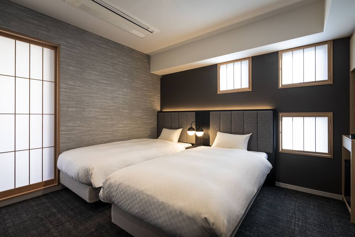A hotel room with two beds, a large window with a view, a wall-mounted lamp, and a wooden headboard.