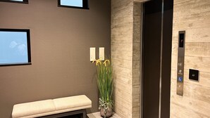 En moderne elevator med træpaneler, en bænk og en potteplante med gule blomster.