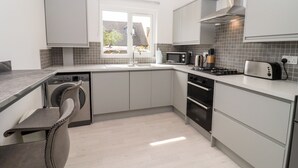 A modern kitchen with a built-in washing machine, a microwave, a toaster, and a stove. - 3 Granbrook Lane (Chipping Campden)