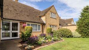 A two-story house with a brick facade, a tiled roof, and a front garden with various plants and flowers. - 3 Granbrook Lane (Chipping Campden)