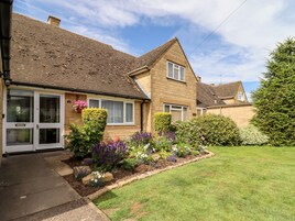 A two-story house with a brick facade, a tiled roof, and a front garden with various plants and flowers.