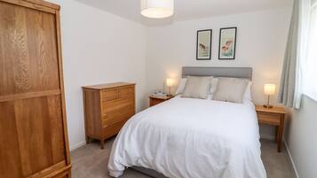 Un dormitorio con cama, armario de madera, mesitas de noche con lámparas y dos cuadros en la pared.
