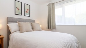 A neatly made bed with a grey headboard, two pillows, and a white bedspread. There are two framed artworks on the wall above the bed. - 3 Granbrook Lane (Chipping Campden)