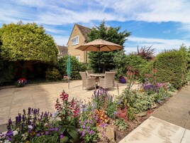 A patio area with a dining table and chairs, surrounded by a variety of colorful flowers and plants.