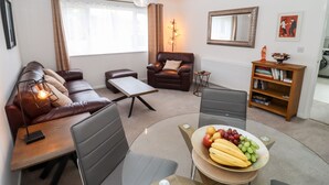 A modern living room with a leather sofa, a coffee table, a dining table with chairs, a bookshelf, and a fruit bowl. - 3 Granbrook Lane (Chipping Campden)