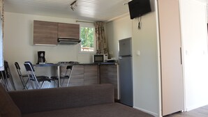 Una kitchenette compacta equipada con microondas, estufa y refrigerador. Hay un sofá y un comedor con sillas. Un televisor está montado en la pared.