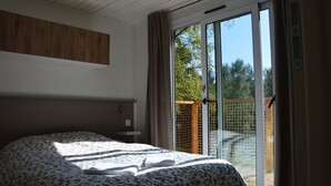 Un dormitorio con cama, cabecera de madera, puerta corrediza de vidrio que da a un área exterior y vistas a árboles y una valla.