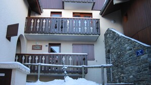 A multi-story building with balconies, a stone wall, and a sign indicating a passage.