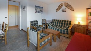 A cozy living room with a plaid sofa, wooden armchairs, a small table, and a red tablecloth.