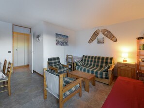 Uma sala de estar acolhedora com um sofá xadrez, poltronas de madeira, uma mesa pequena e toalha de mesa vermelha.