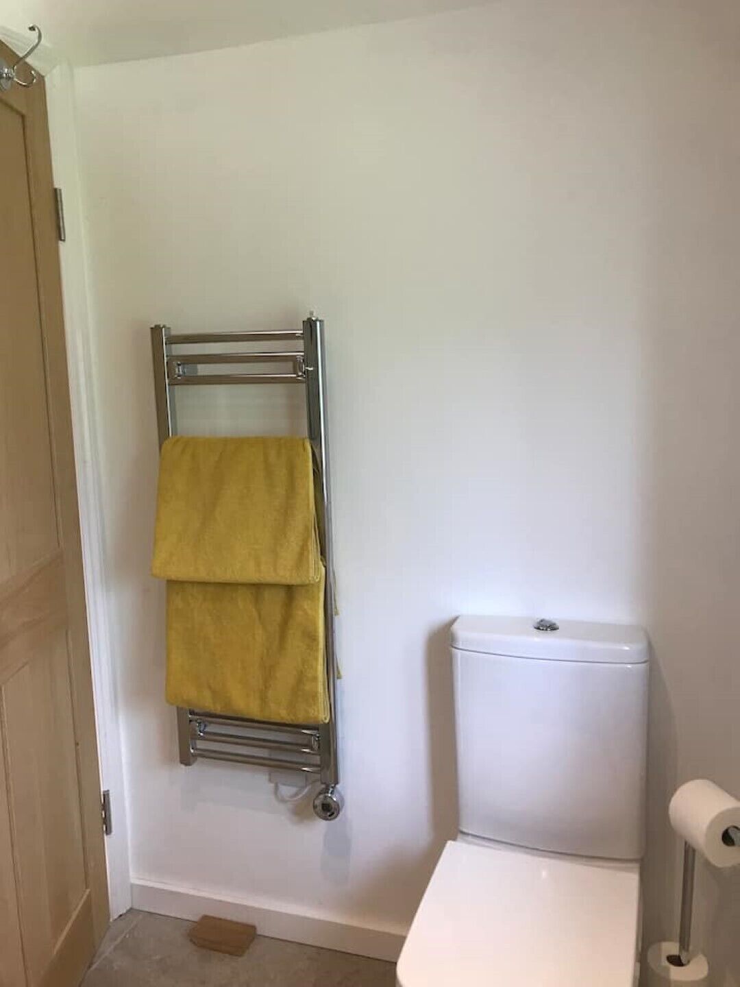 Een badkamer met een wit toilet, een handdoekrek met een gele handdoek, en een toiletpapierhouder.