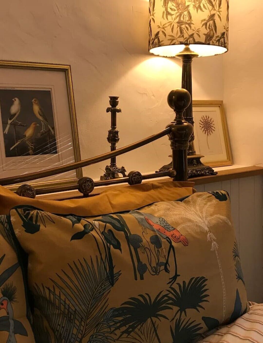 Een bed met een bloemenkussen, een lijst met een afbeelding van vogels, een lamp en een decoratief wandobject.