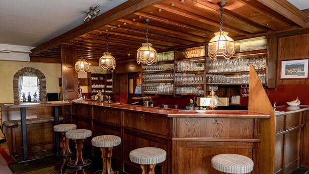 Una zona de bar con taburetes de madera, lámparas colgantes y estanterías con copas.