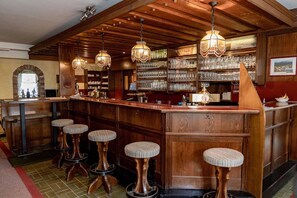 Een bar met houten barstoelen, hangende lampen en planken met glazen.