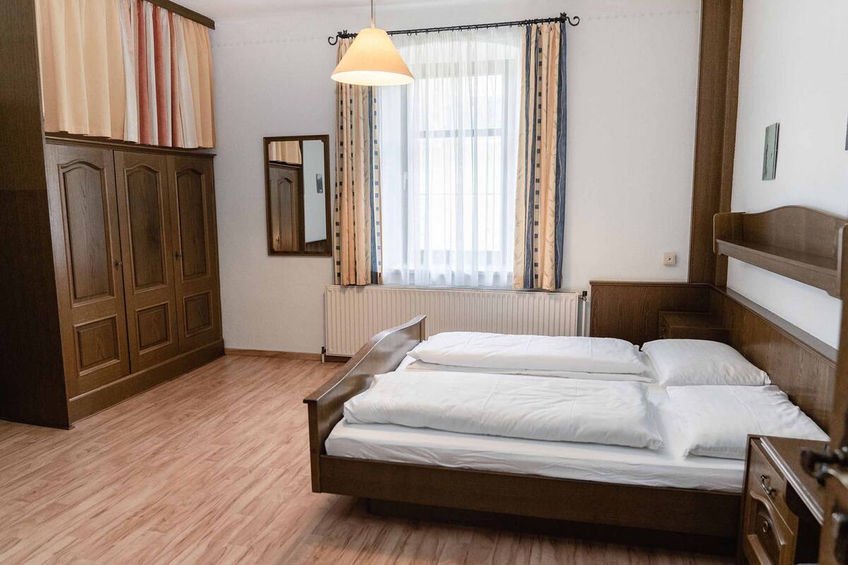 Un dormitorio con una cama de madera, un radiador, una ventana con cortinas, un espejo y un armario.