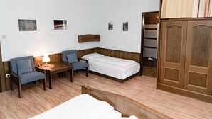 Una habitación con cama, dos sillas, una mesita con lámpara, un armario de madera y una lámpara colgante.