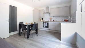 Una cocina moderna con armarios blancos, horno empotrado y comedor con mesa y sillas.