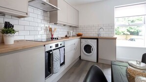 Una cocina compacta con armarios blancos, horno empotrado, lavadora y ventana que proporciona luz natural.
