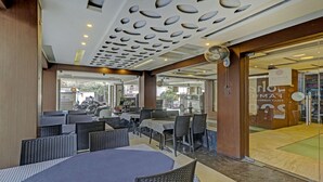 An indoor seating area with round tables and chairs, a ceiling with a unique pattern of oval cutouts, and a glass door leading outside. -  Loharkar Hotel (Nagpur)