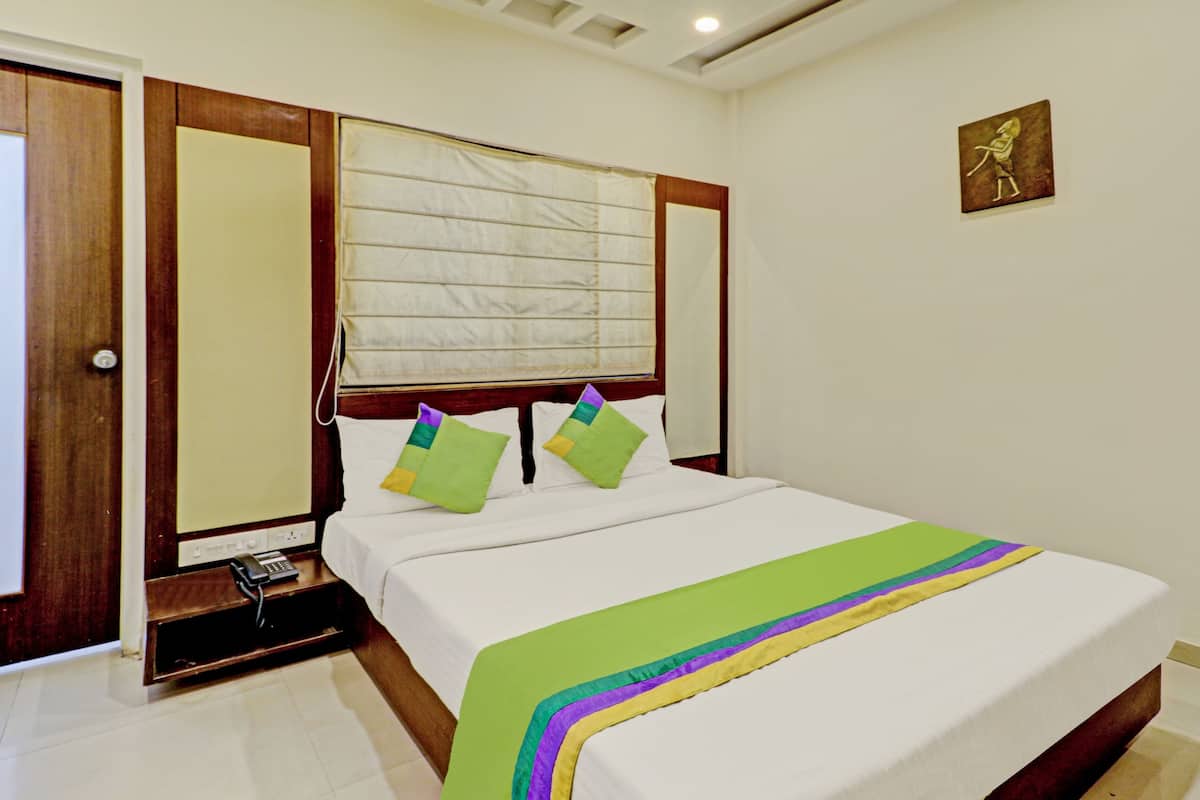 A hotel room with a bed, a bedside telephone, and a window with blinds.