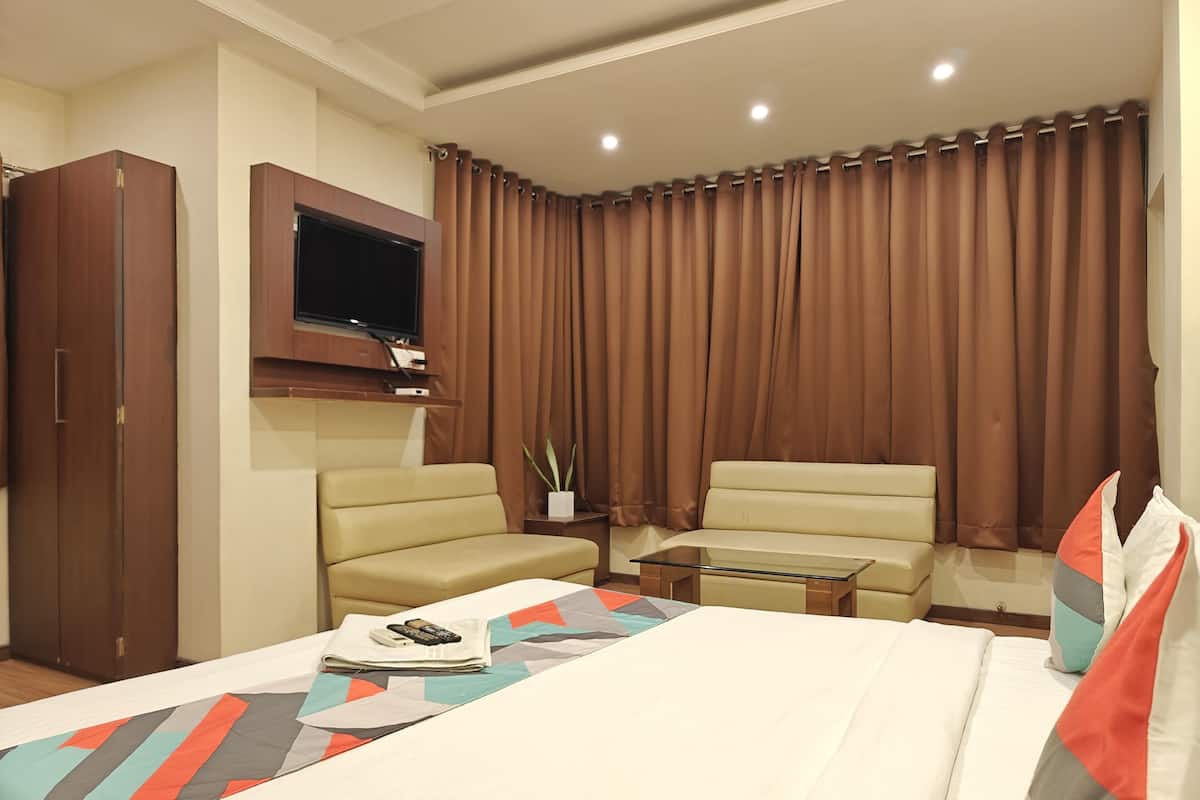A hotel room with a bed, two sofas, a TV, and a window with curtains.