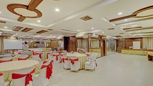 A banquet hall with round tables, white chairs with red sashes, and a stage with a white screen. -  Loharkar Hotel (Nagpur)