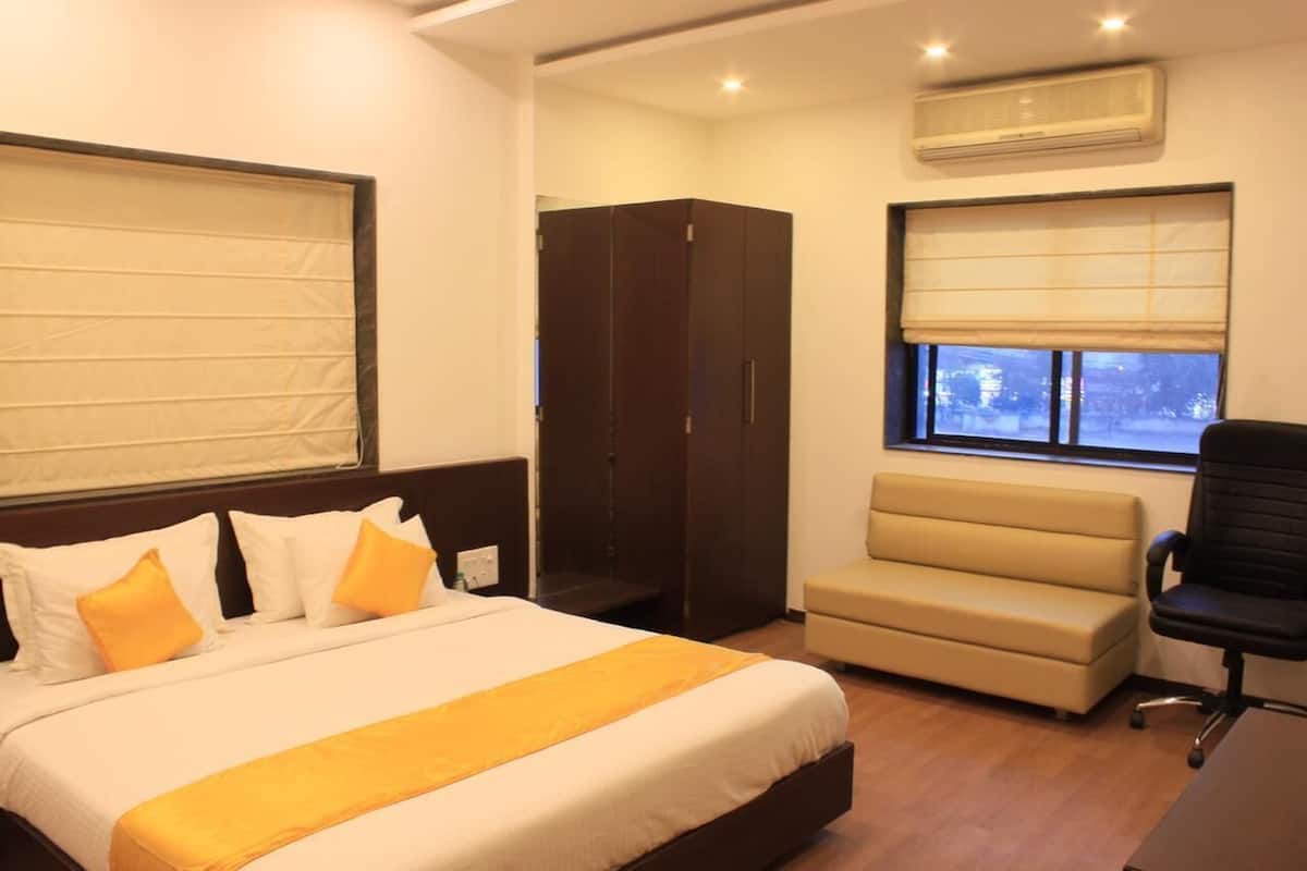 A hotel room with a bed, a wardrobe, a sofa, a desk, and a window with blinds.