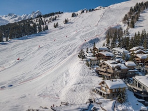 Ein Skigebiet mit mehreren Holzhäusern, Skipisten und freiem Blick auf die umliegenden Berge.