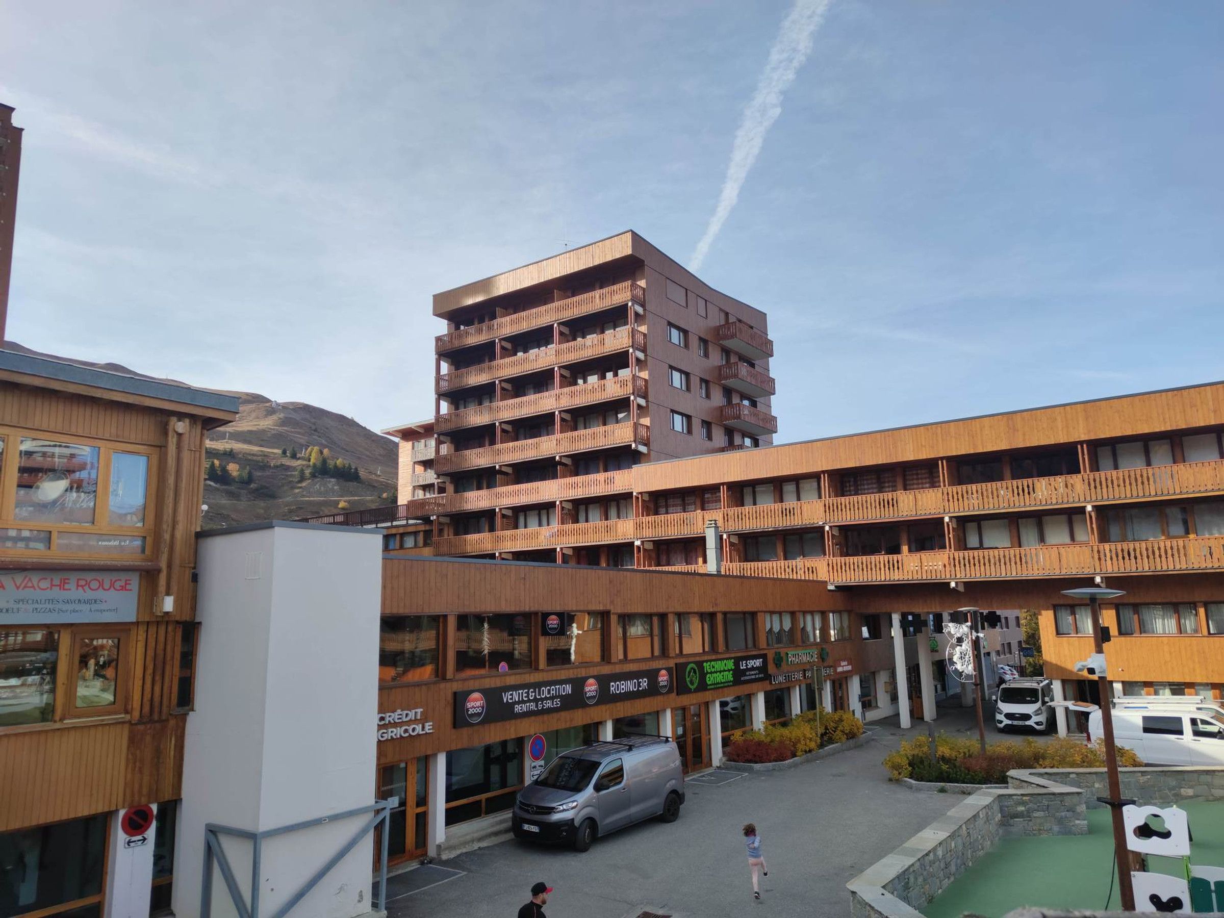 Un edificio a più piani con balconi, un'area parcheggio e un cartello per un servizio di autonoleggio.