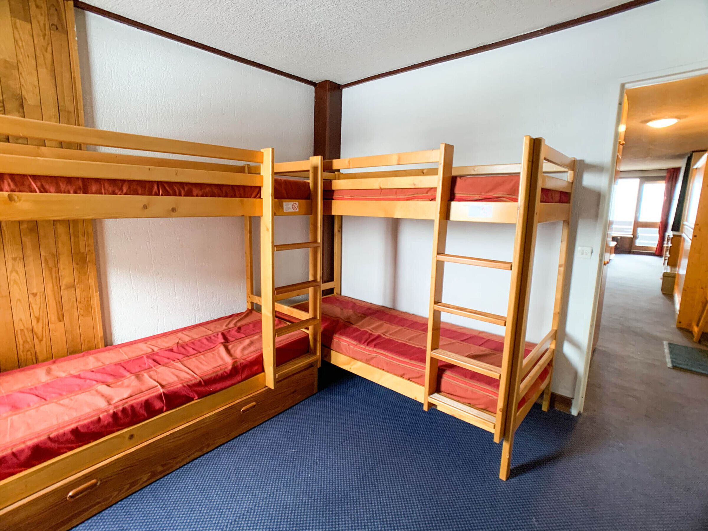 A bunk bed room with a blue carpet, wooden walls, and a door leading to another room.