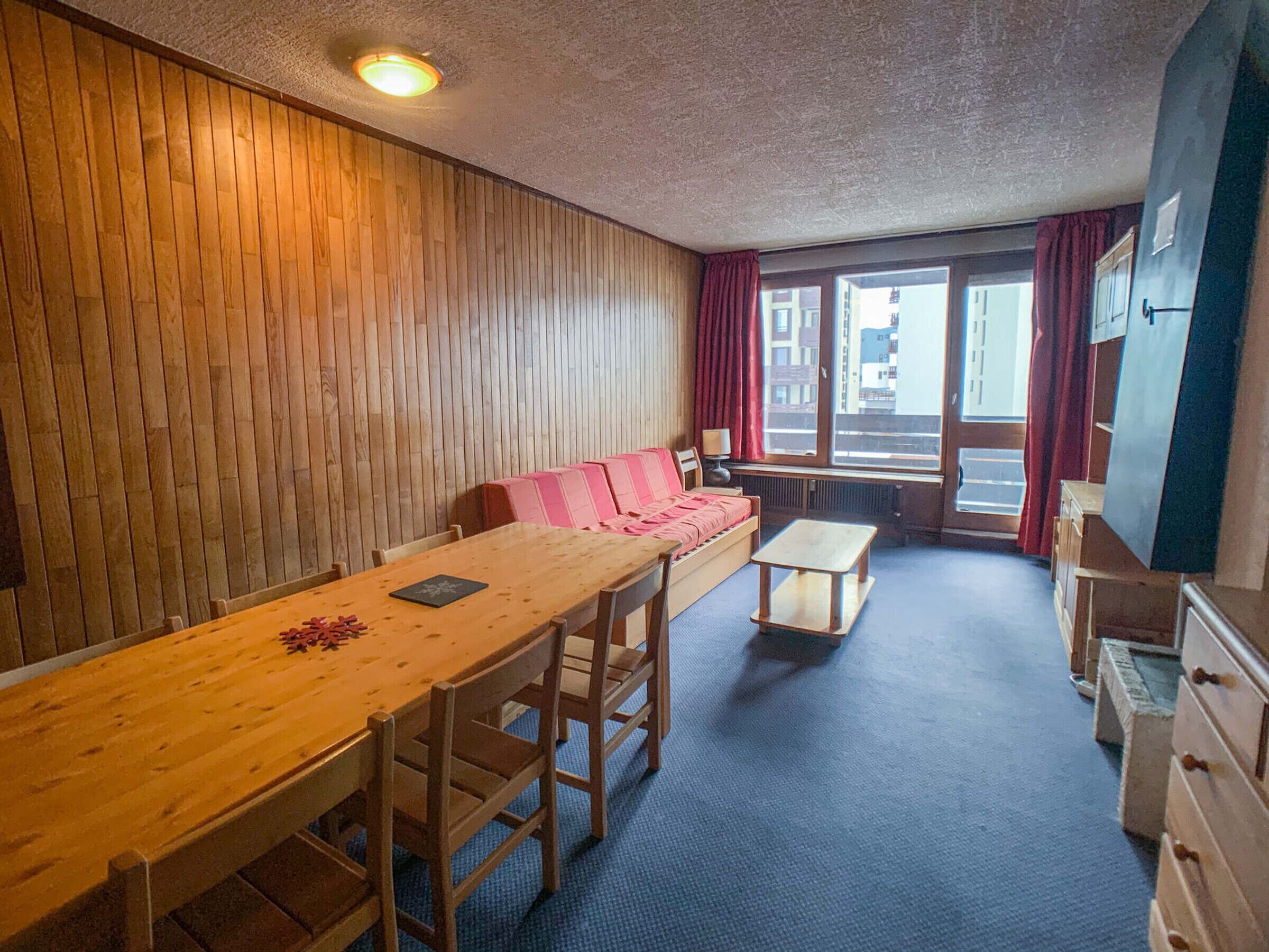 A room with a wooden table, a sofa, and a window with curtains.