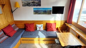 Una camera accogliente con un letto di legno, un tavolino e una sedia. Ci sono due cuscini, uno con un motivo cervo, e una lampada a parete.
